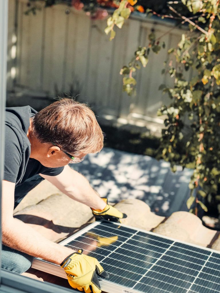 An adult male installing a solar panel on a rooftop, highlighting clean energy technology.